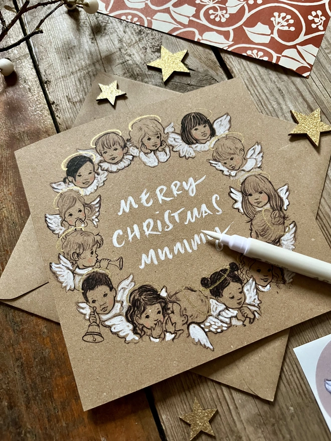 a kraft card Christmas card featuring a vintage storybook style illustration of a wreath of angels