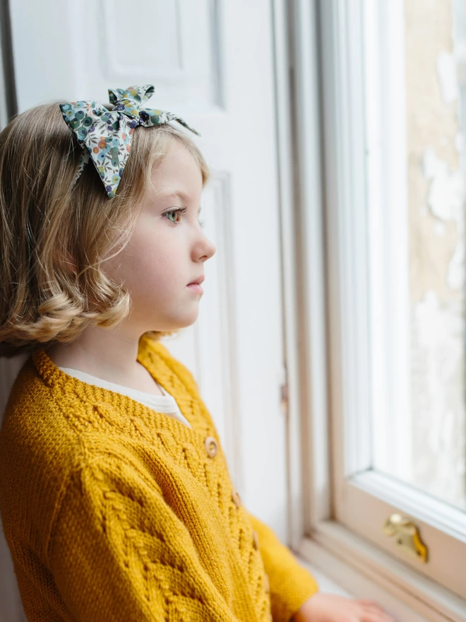 little girl looking out of window wearing a liberty alice band