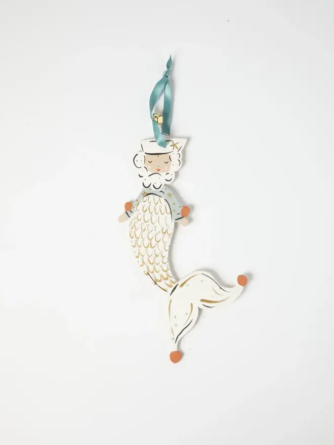Merman Tree Dancer. a flat lay product shot of the merman tree dancer hanging ornament on a plain white background, showing a bearded merman figure in a sailor hat and striped teal top, with a cream scale-patterned tail edged in gold. the tail curls into a jester-style pointed tip with orange-tipped ends, and the figure hangs from a teal ribbon with a small gold bell attached. hand-painted detailing gives the ornament a folk-art, storybook charm.