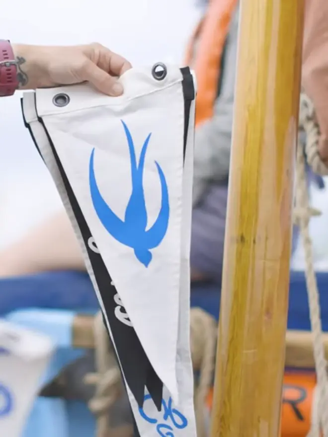 somebody holding up an ivory pennant flag with a blue swallow stitched on.