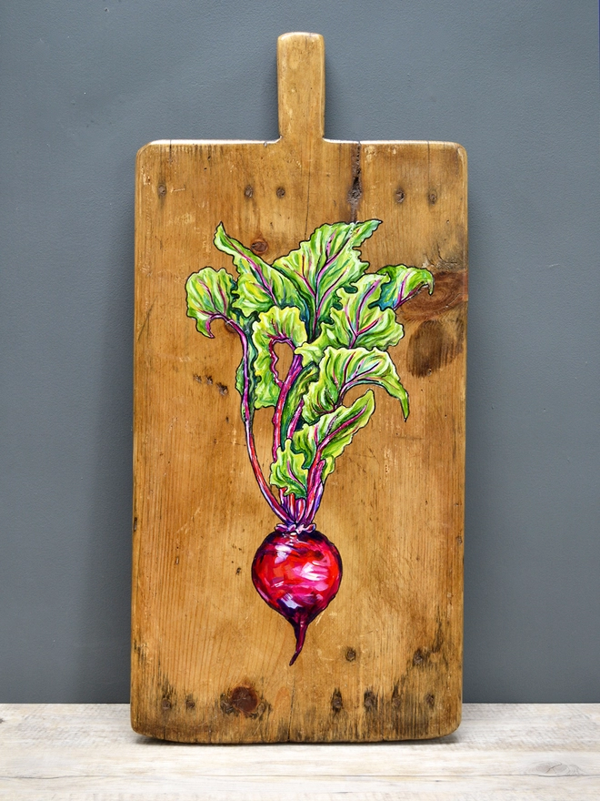 Wooden chopping board with handpainted design of a beetroot standing against a wall