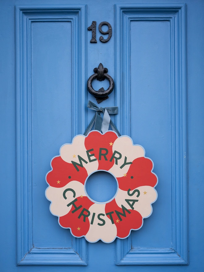 Red and pale pink Hand painted Christmas Wreath with gold leaf stars on a blue front door