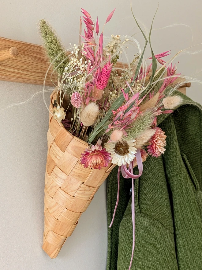 wooden braided cone basket with dried pink flowers hanging on a black wall