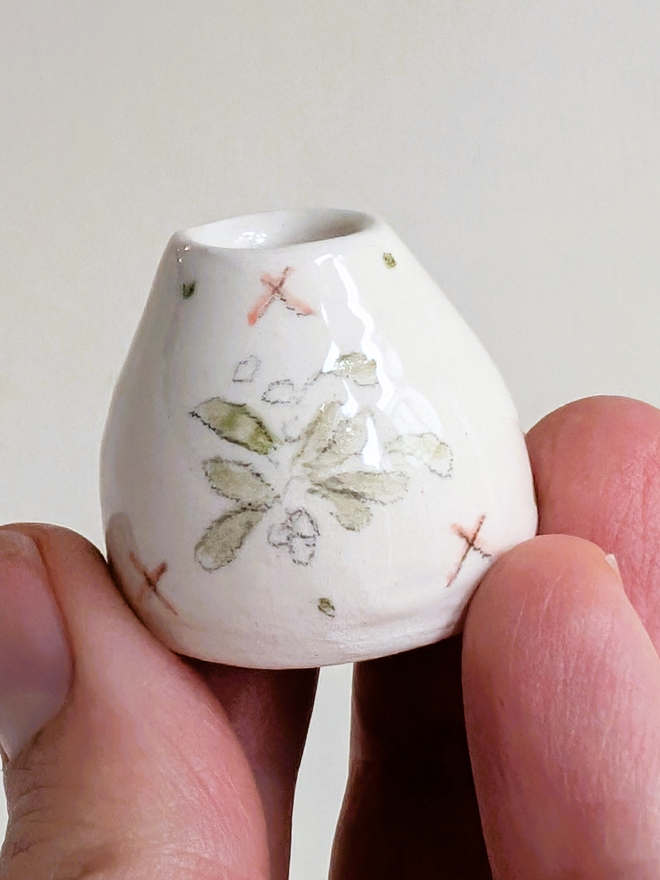 Miniature vase with hand painted mistletoe held in fingertips