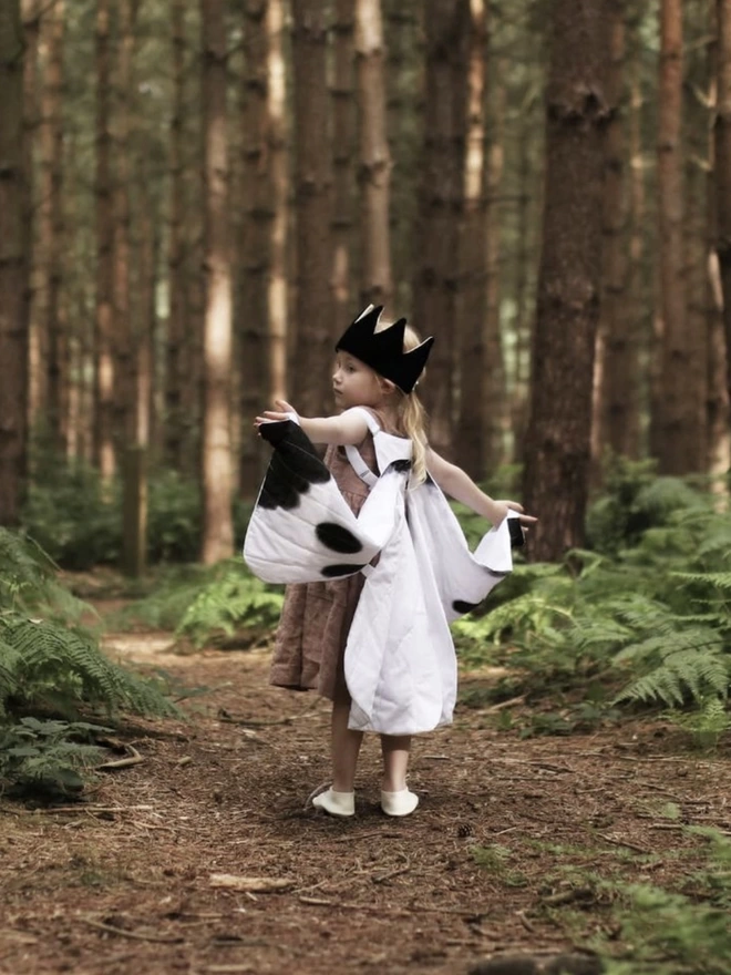 a child stood in a forest wearing a black and white butterfly wings costume and a black crown