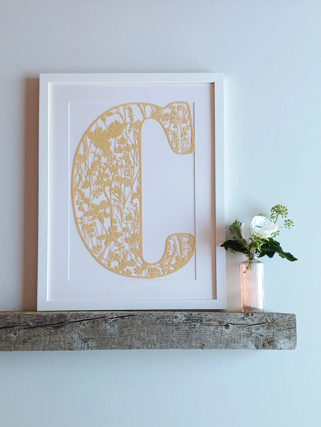 Spring Initial Papercut Letter C in pale yellow, framed in narrow white frame displayed on shelf