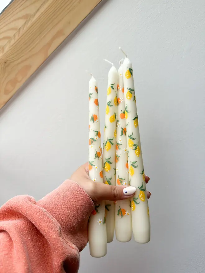 Lemon Zesty & Orange Bloom Hand Painted Candles, a woman holding a group of lemon and orange taper candles in her hand above a floor. 