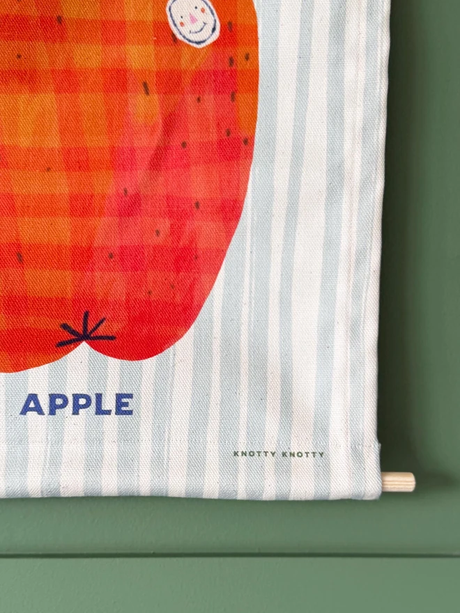 Cotton Apple Wall Hanging, against a green wall. 