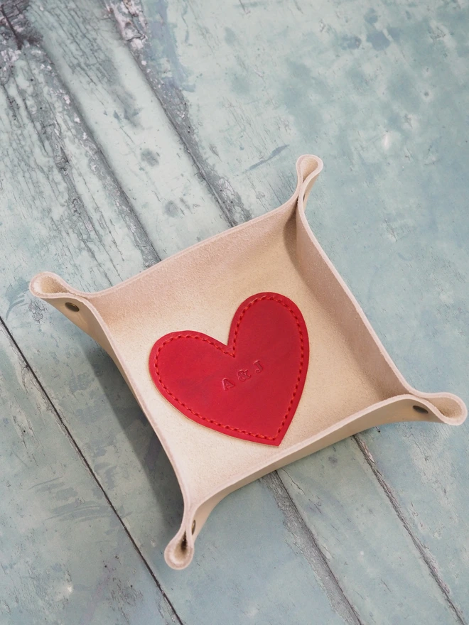 Personalised leather coin tray with love heart base. A handmade natural cream square leather tray with a red love heart in the base. The love heart has been stamped with initials for a wedding anniversary gift.