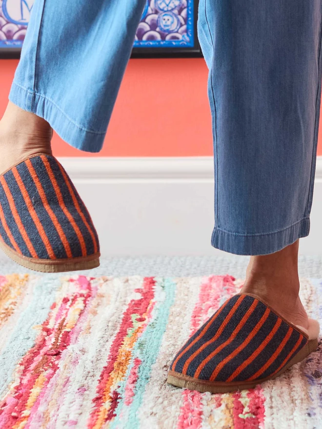 Lambswool & Sheepskin Slippers, a pair of colourful lambswool and sheepskin slippers sitting modelled in front of a colourful wall. 