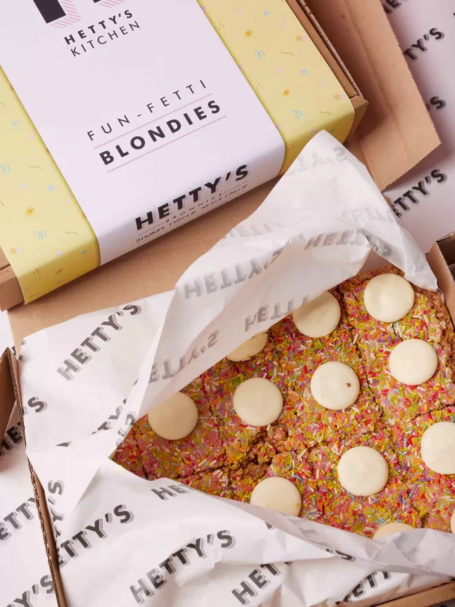 Ten slice Funfetti blondies with sprinkles and white chocolate buttons in the branded packaging it will arrive inside