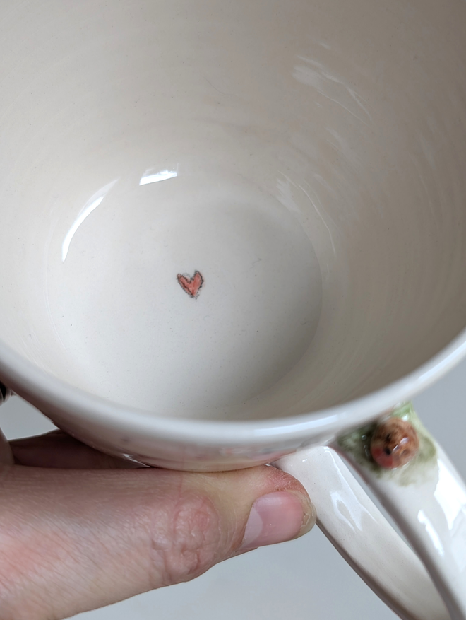 ivory ceramic cup with a tiny pottery robin on the handle and red heart on the inside