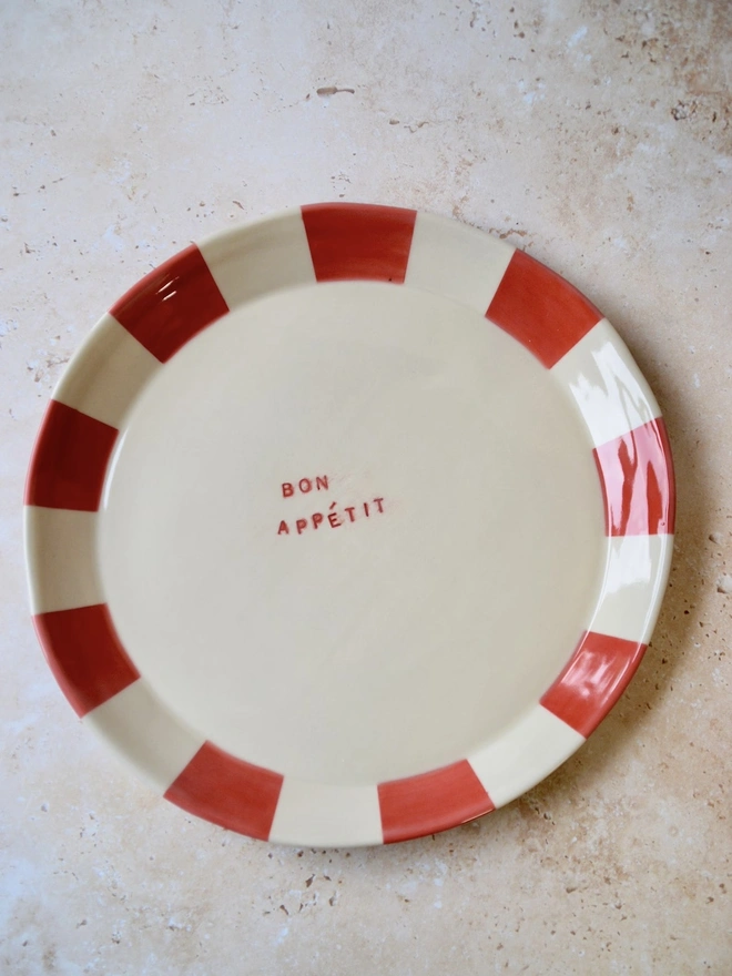 Handmade ceramic plate with red and cream striped rim — “Bon Appétit” text in centre