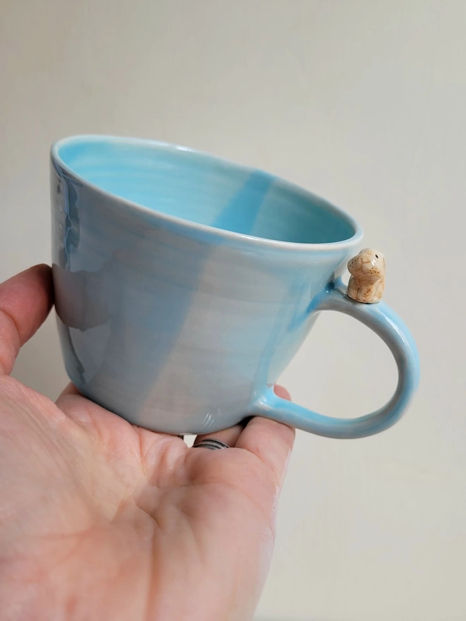 Blue translucent glazed pottery cup held in a hand with a tiny cute rabbit on the handle