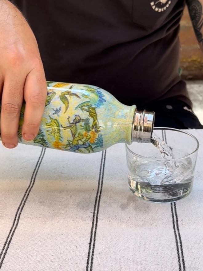 Man pouring from dinosaurs sustainable insulated charity water bottle in blue & yellow illustrations