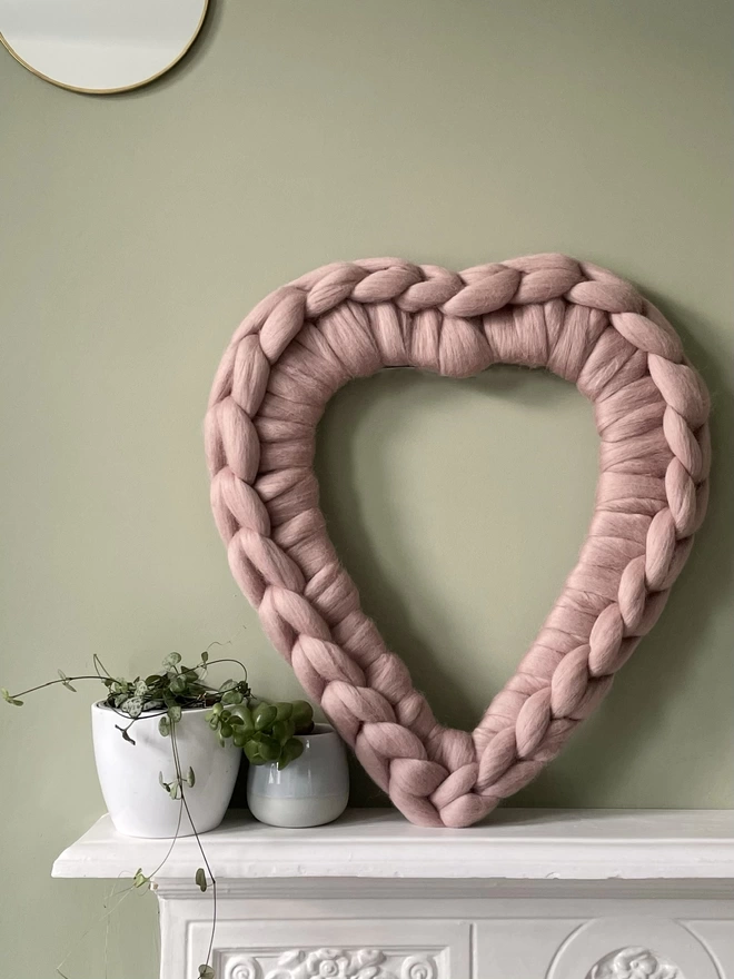 A mink pink woolly heart wreath sitting on a white mantel