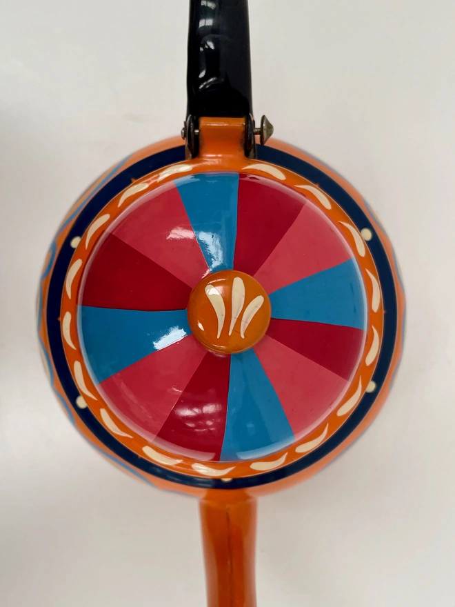 Lid or orange teapot featuring a pink, red and blue striped design. 