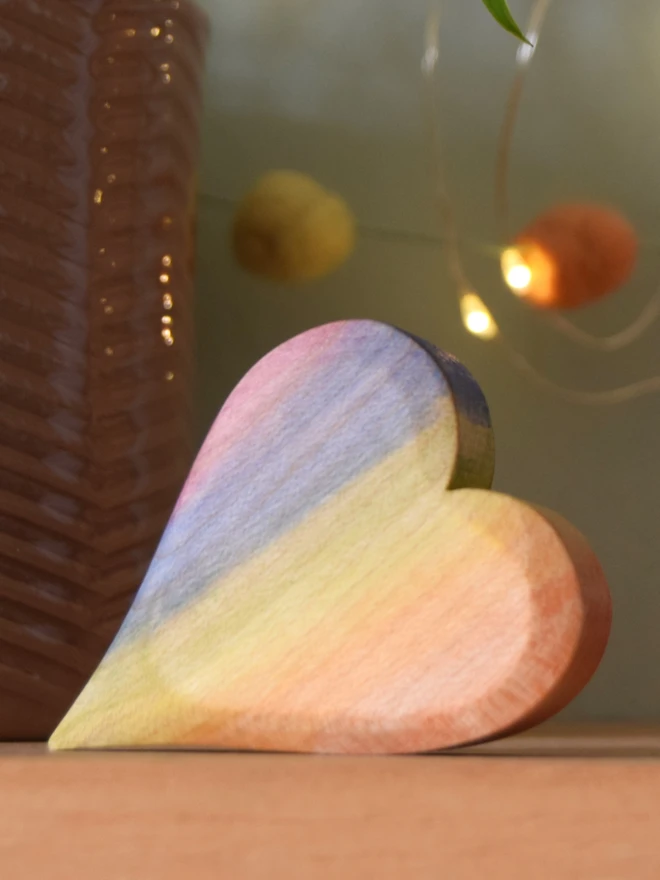 wooden rainbow heart on a shelf with lights behind