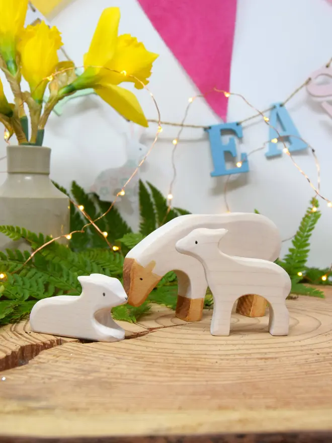 wooden toy white sheep and lamb family set on wood slice with daffodils and easter bunting behind