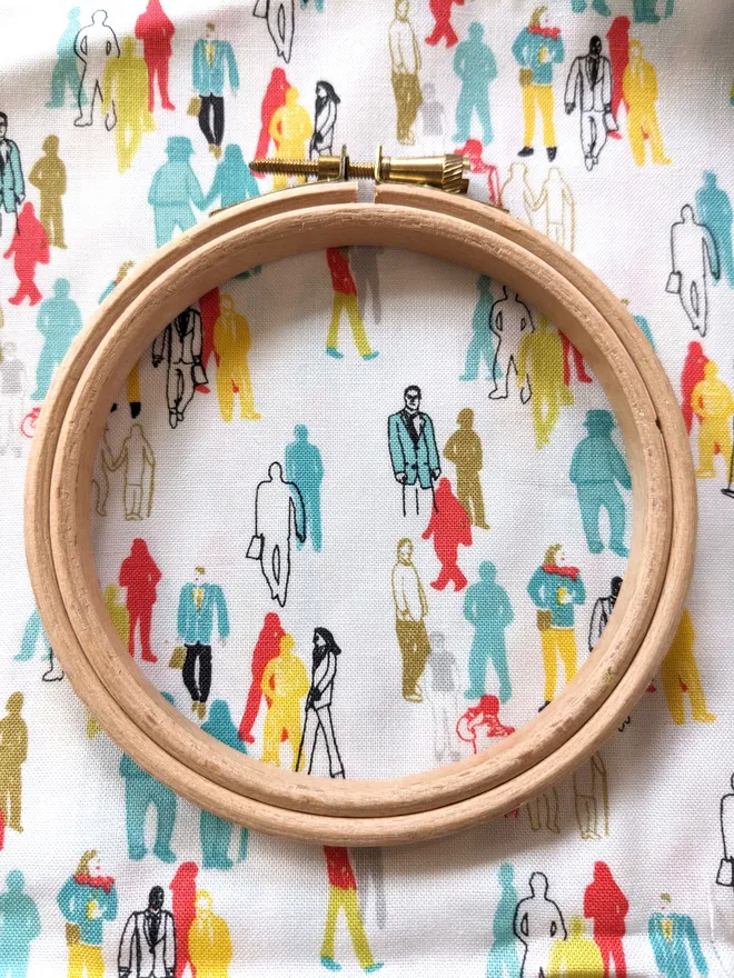 A wooden embroidery hoop lying on fabric with a crowds design