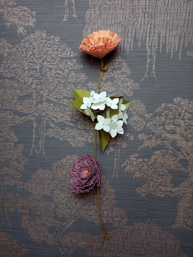 a trio of paper flowers, hanging on a wall like a daisy chain