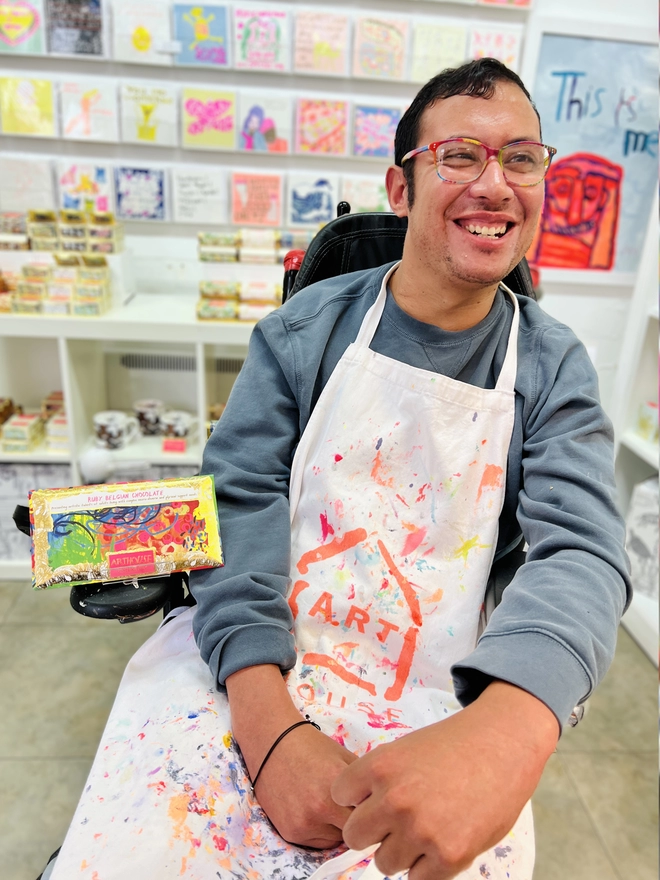 Artist holding charity ruby chocolate bar wrapped in foiled card & bright colourful abstract design 