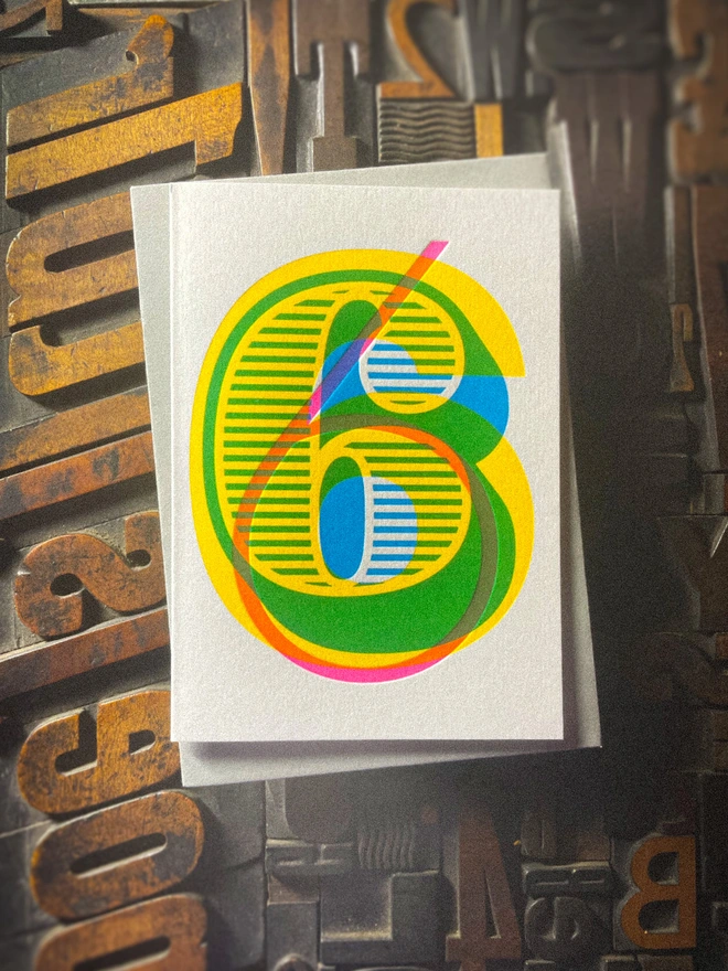 Handmade letterpress 6th birthday card featuring bold overlapping numerals printed in vibrant fluorescent cyan, magenta and yellow inks. Each card is individually hand printed using traditional letterpress techniques on luxury paper stock, creating a beautifully tactile finish with a deep impression and rich layered colours inspired by the CMYK printing process. Printed on a traditional letterpress from 1915.