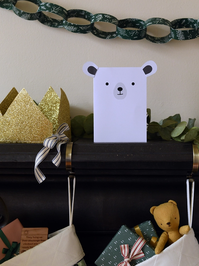 A white polar bear Christmas card with stick on ears stands on a black mantlepiece. 