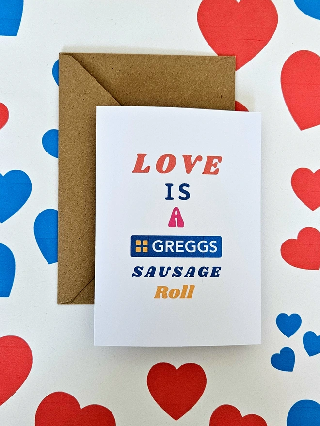 A photograph of the front of a humorous A6 greeting card illustrated using brightly coloured text. The text says love is a Greggs sausage roll 