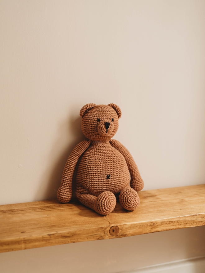 handmade brown crochet teddy bear on wooden shelf