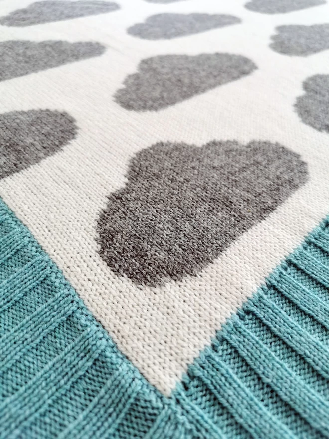 Close up of corner of baby blanket showing knit stitches, ribbed trim and cloud pattern