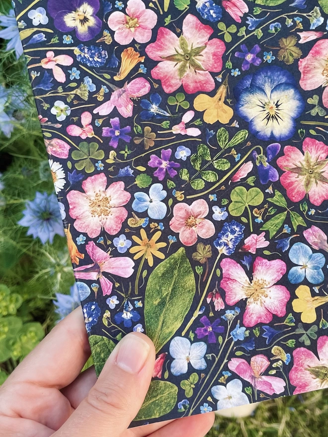 Close-Up Detail of Hand Holding Notebook with Pressed Flower Cover, Garden in Background
