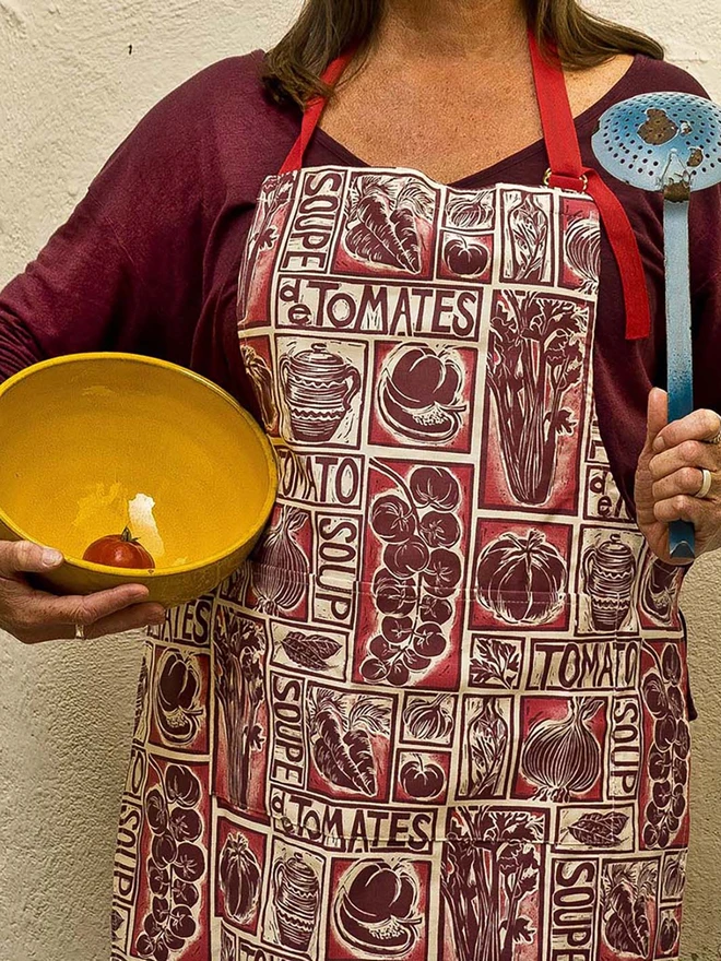 Lady wearing a Kate Guy Linocut tomato soup recipe apron with bowl and ladle