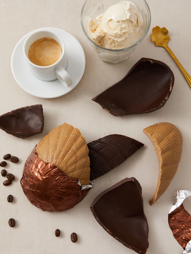 affogato coffee chocolate easter egg. a coffee chocolate easter egg photographed partially unwrapped from bronze foil with coffee, ice cream and coffee beans.