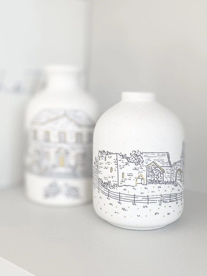Two ceramic vases with a black line drawing of a wedding venue