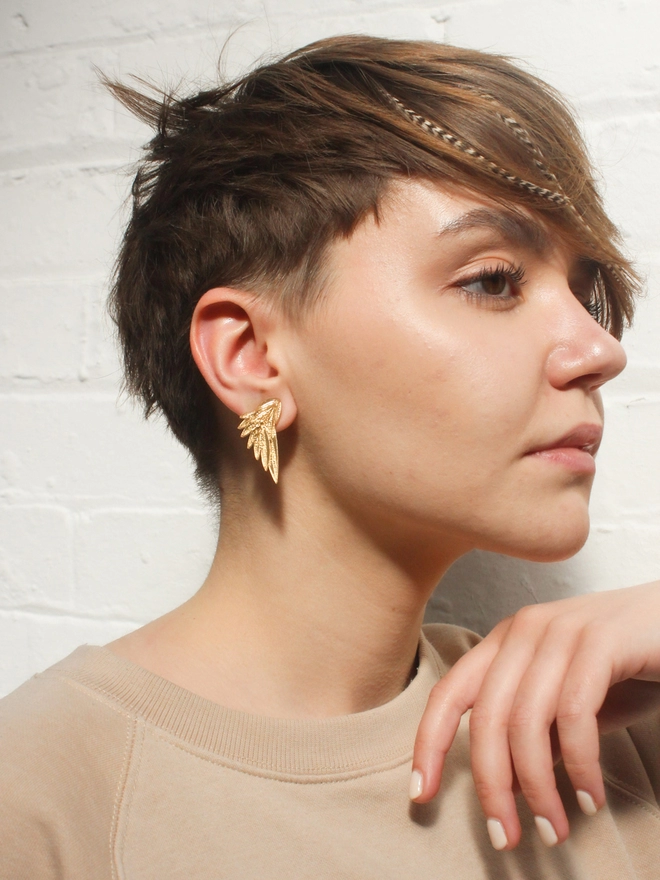 A woman earring Wing shaped Earrings in Gold Acrylics with a camel coloured jumper.