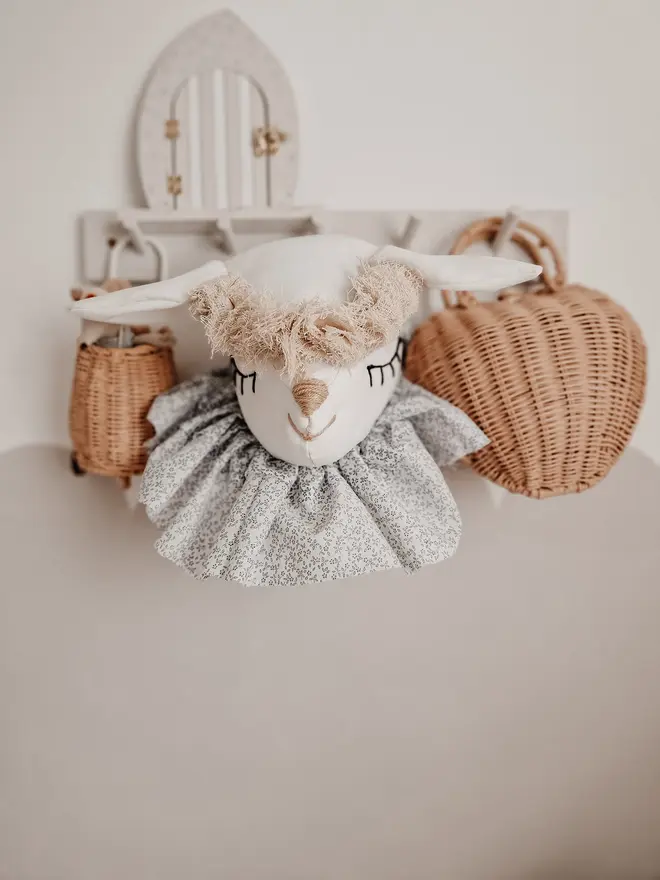 Sheep Head Wall Mount, a hanging sheep head decoration sitting against a plain wall in child's bedroom. 