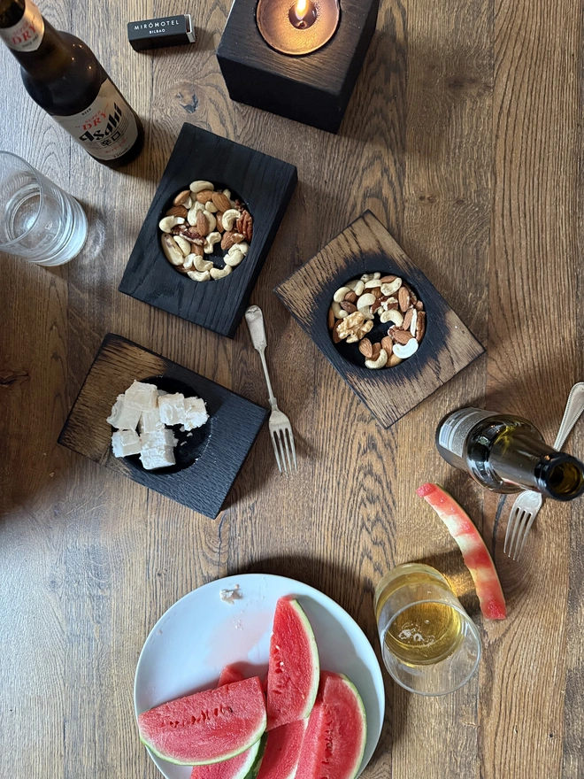 Charred wood nibble bowls with nuts cheese and beer.