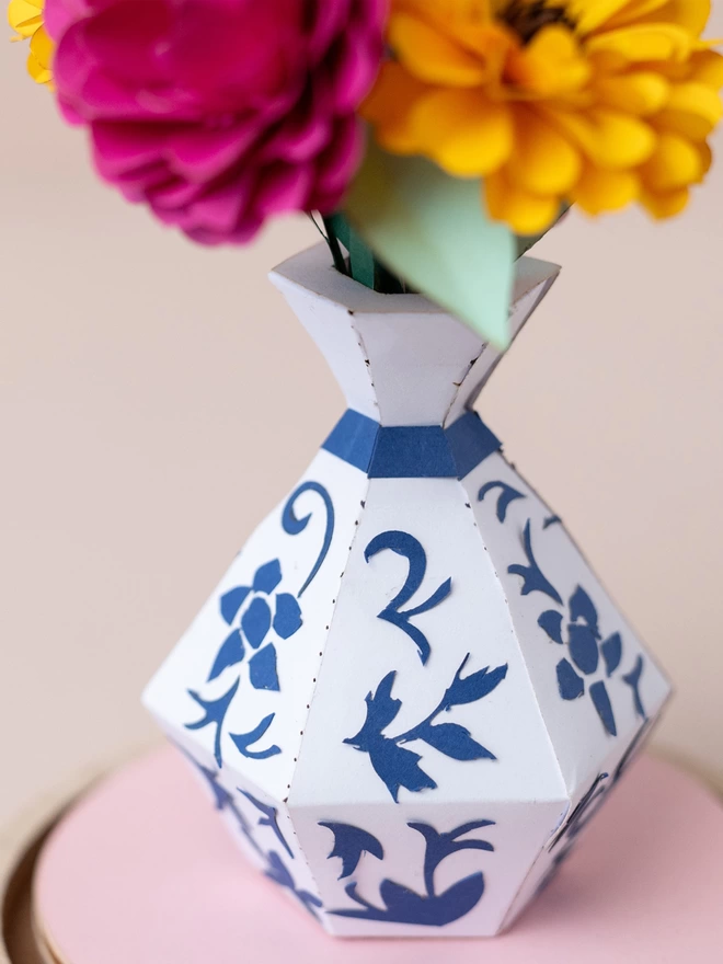 a bunch of paper flowers in a white and blue vase . This is a craft kit by My papercut Forest