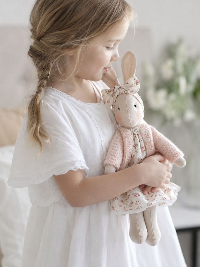 Little girl holding linen bunny doll with ditsy dress and  pale pink cardigan 