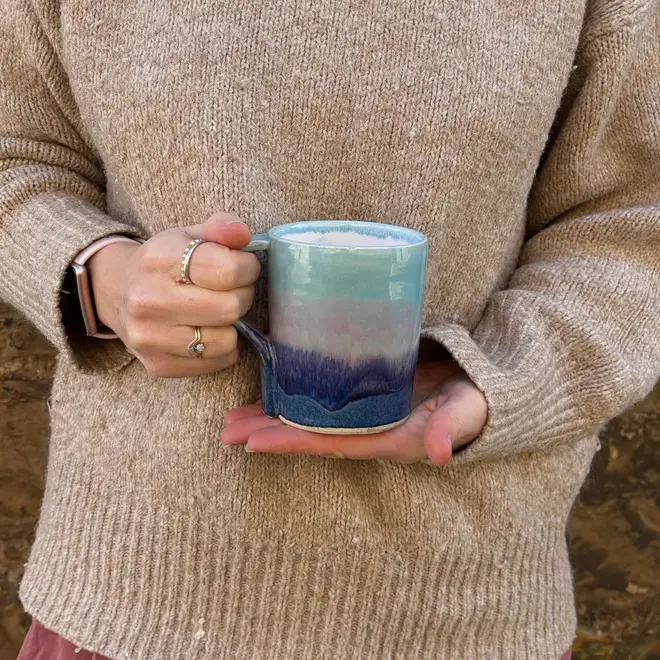 Landscape Standard Mug, a person wearing a jumper holding a colourful mug in front of them. 