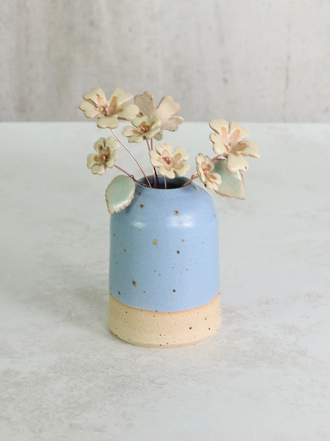 small blue handmade stoneware vase featuring an arrangement of ceramic primroses in two sizes, flowers are a pale yellow like the wild primrose
