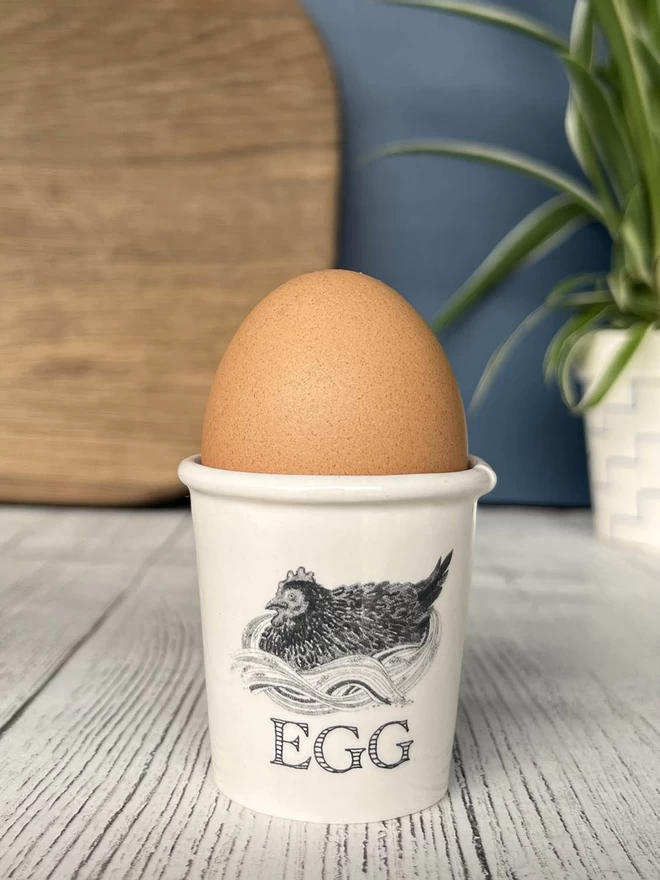 A handmade egg cup, emulating a paper cup, is decorated with an illustrations of a plump hen.