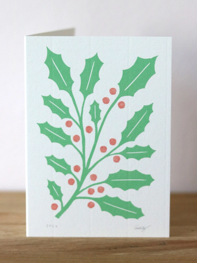 A Christmas card featuring a reproduction of an original linocut print of holly