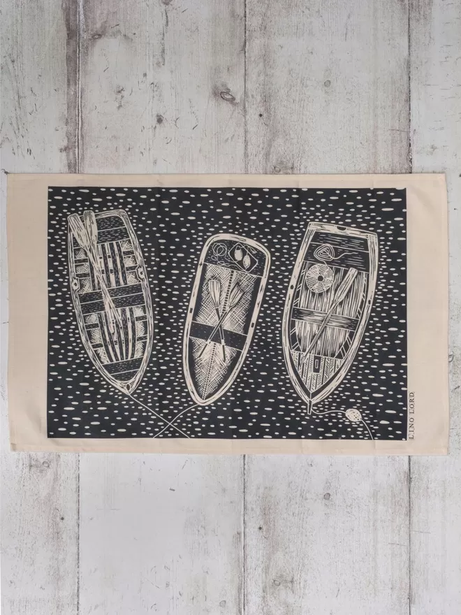 Picture of a tea towel with an image of 3 rowing boats, taken from an original lino print