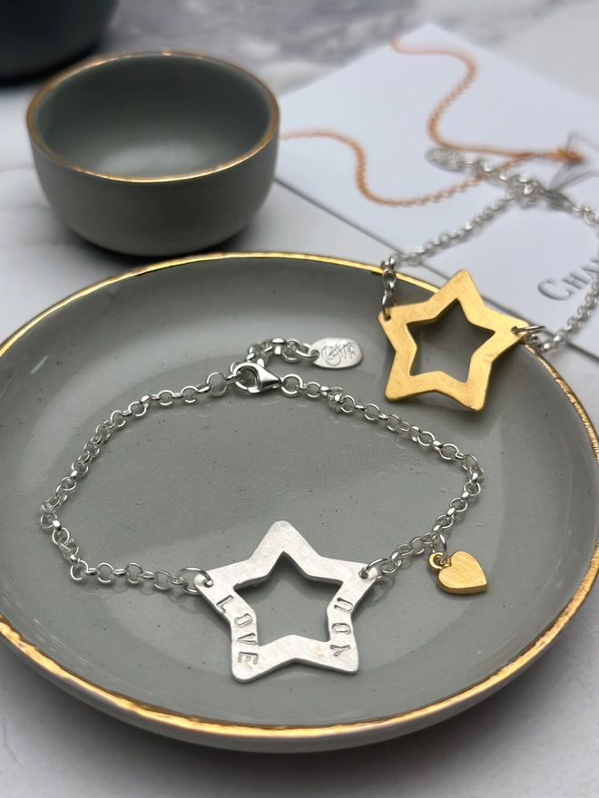 personalised sterling silver open star charm on a silver belcher chain bracelet with additional tiny heart charm in gold. also a gold version of the bracelet in the background