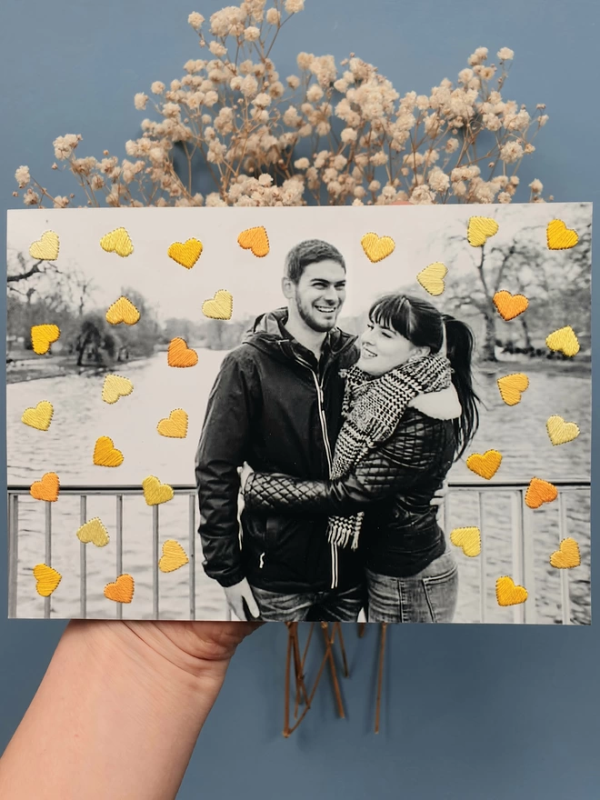 Couple photo in B&W, with hand embroidered shades of yellow hearts held against blue background