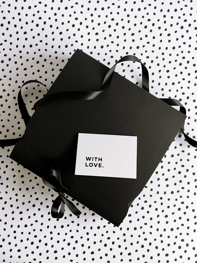 Black gift box tied with a ribbon with a 'with love' notecard laid on top.