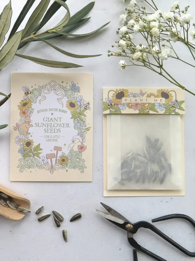 A cream "Giant Sunflower Seeds, Sow a Little Sunshine" card framed with sunflowers, bees and butterflies. Next to it is a glassine pouch of sunflower seeds under a floral "Plant Me" topper.