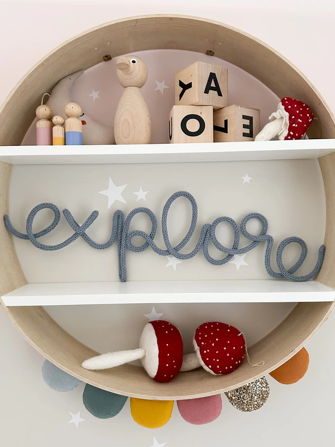 'explore' motivational sign for kids propped up and displayed on a circular shelf with other fun and modern children's decorations.
